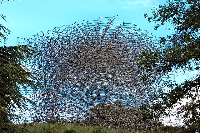 The Hive, a lattice of aluminium rods forming a glittering dome, framed by cedar branches against a blue sky