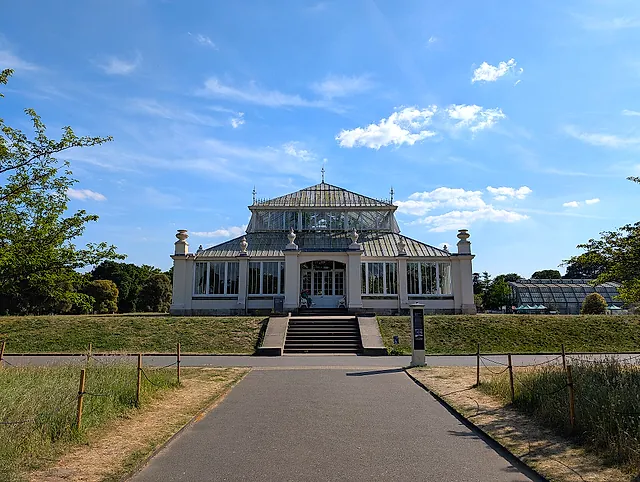 La Temperate House vista di fronte dal viale d'accesso, con la scalinata verso l'ingresso centrale e il cielo azzurro