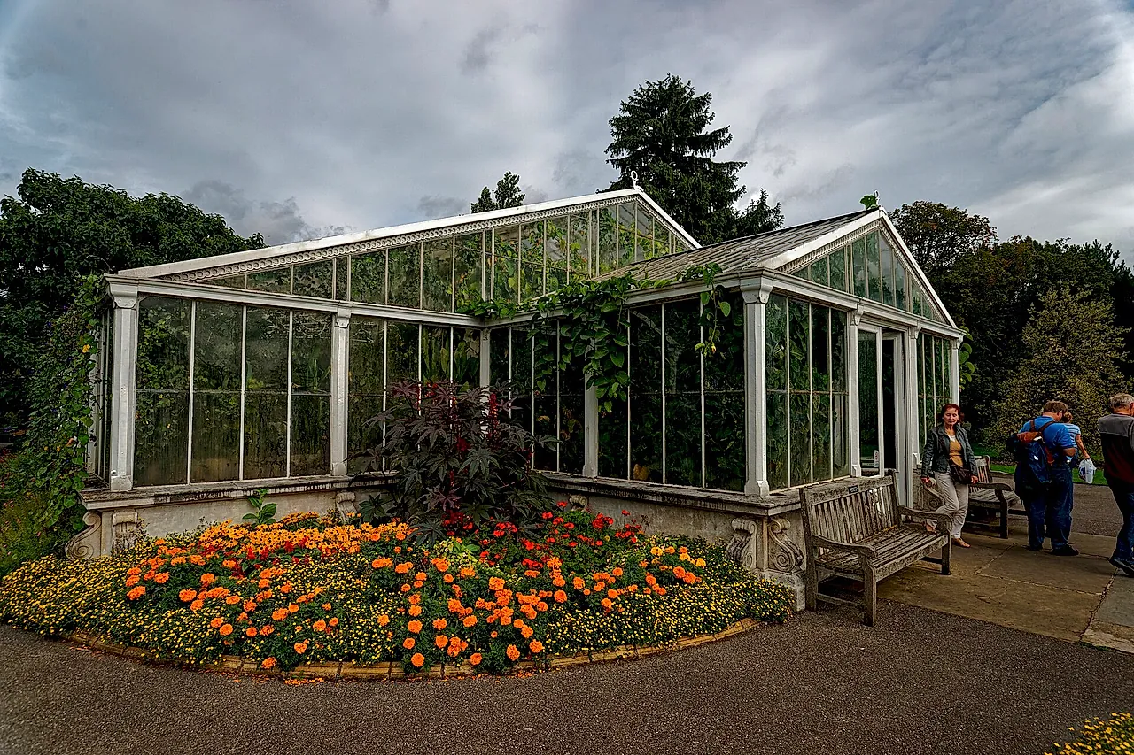La Waterlily House di vetro con un'aiuola di tagete arancioni ai piedi e il cielo nuvoloso